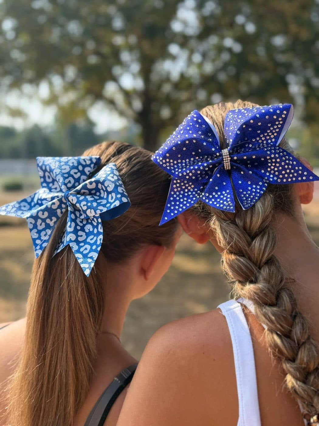 Zwei Cheerleaderinnen von hinten, eine mit blauer Leo-Print-Schleife, eine mit royalblauer Strass-Schleife