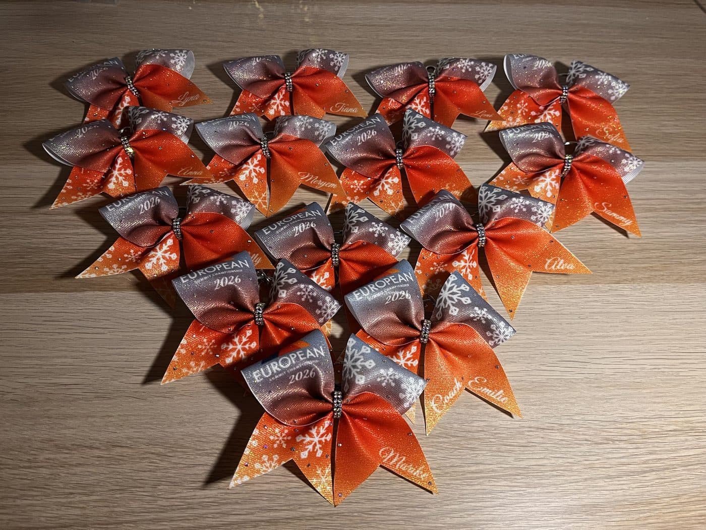 Team-Set aus orange-grauen Schleifen mit Schneeflocken, dem Aufdruck „European Championship 2026“ und je einem Namen