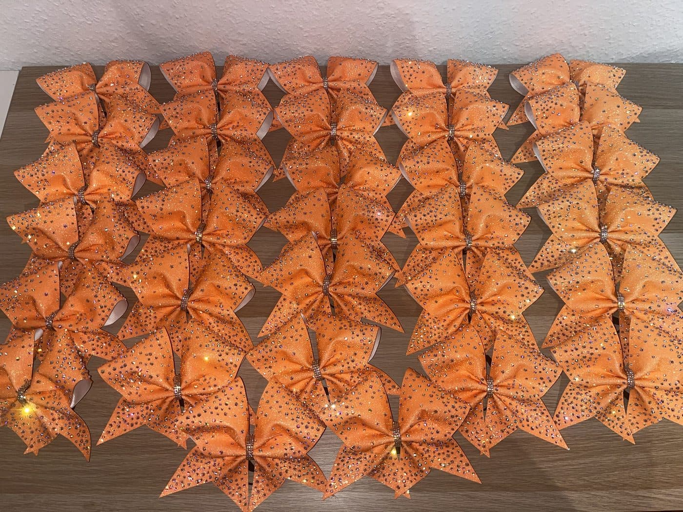 Rund dreißig orangefarbene Glitzer-Schleifen mit Strass, in Reihen ausgelegt