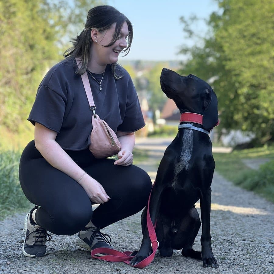 Selina hockt auf einem Feldweg und schaut ihren schwarzen Hund Odin an